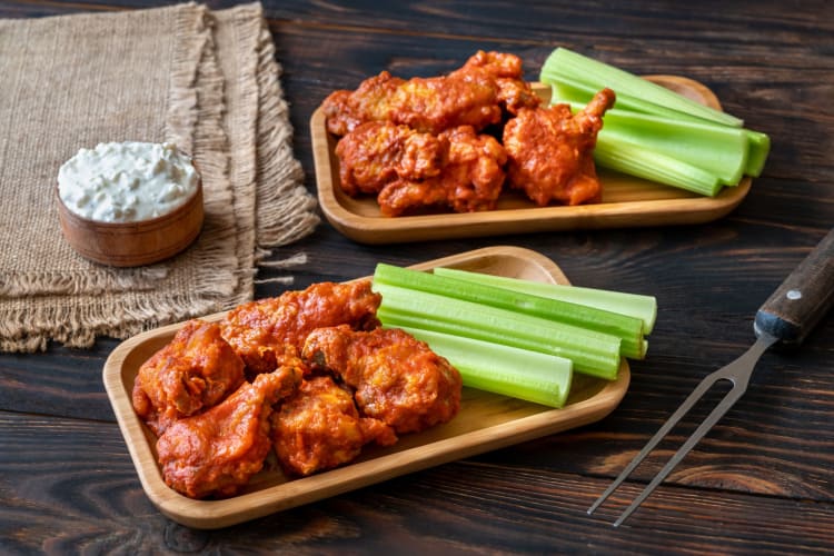 Two plates of chicken wings with blue cheese dressing and celery sticks.