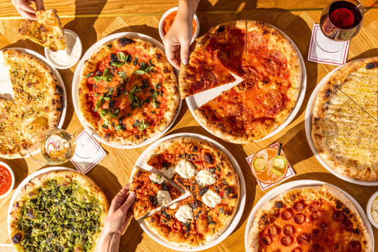 People taking slices from a selection of pizzas on a table