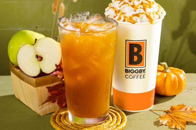 A glass of cider and a whipped cream-topped drink next to apples