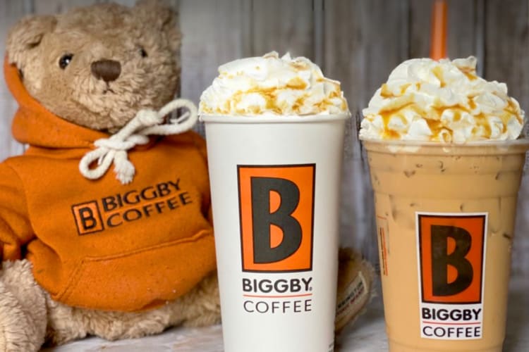Two caramel coffee drinks next to a teddy bear in an orange hoodie