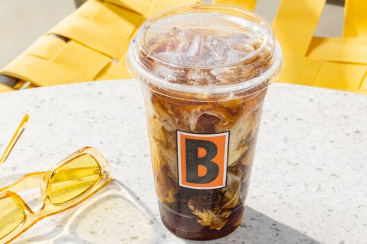 An iced coffee on a table next to yellow sunglasses