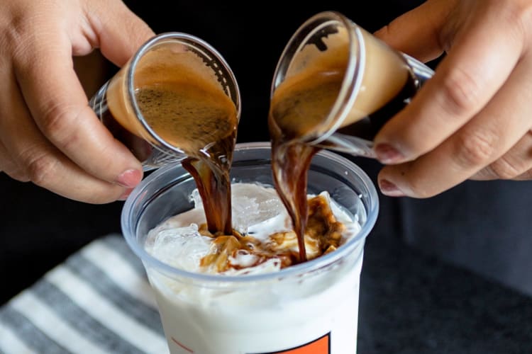 A person pouring two shots of espresso into milk
