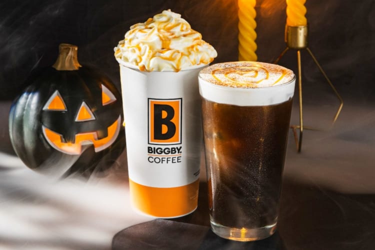 Hot and iced Halloween coffee drinks next to a pumpkin decoration
