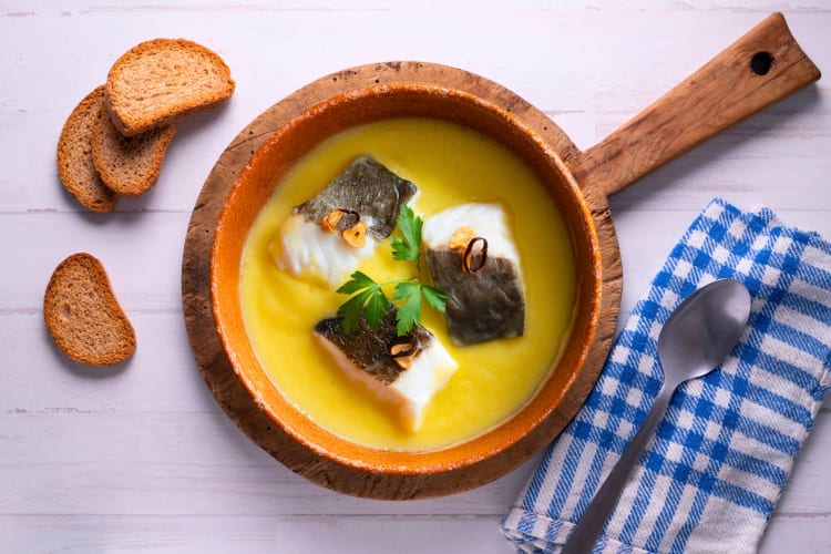 A bowl of fish stew next to bread
