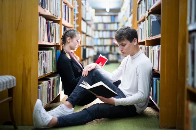 A couple sitting on the floor reading books in a library