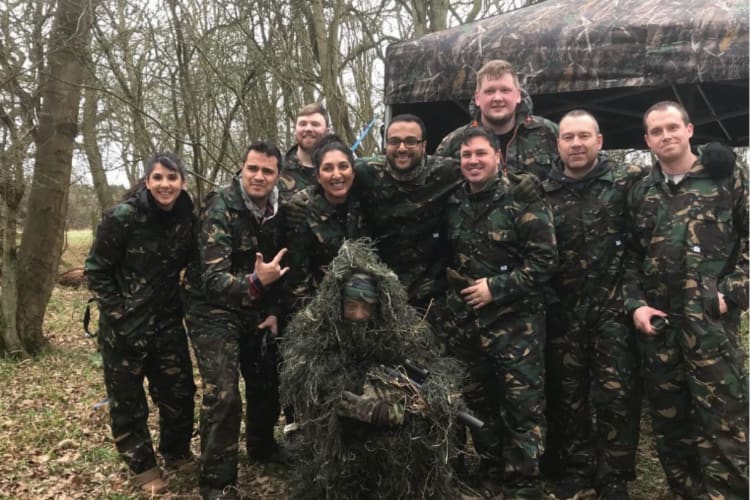 a group of smiling friends in camouflage clothing stand in a wood