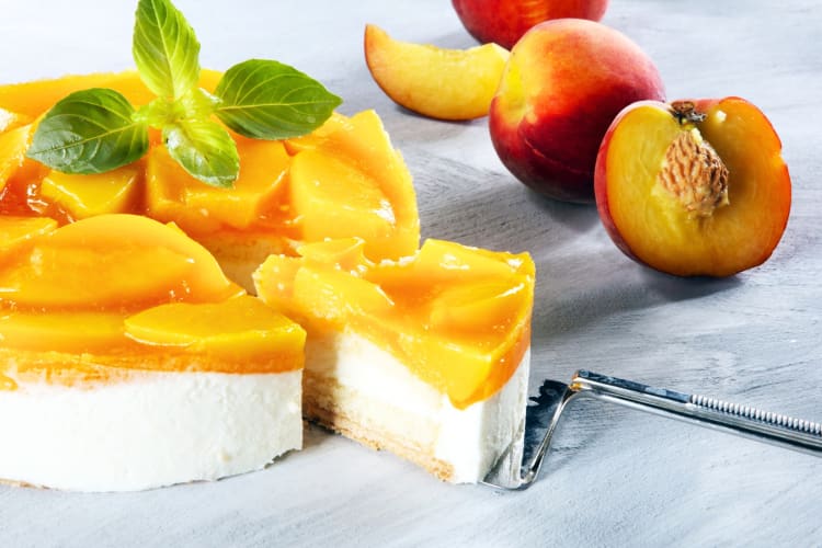 A cheesecake with peaches next to fresh peaches