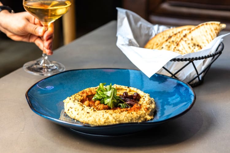 Hummus and pita next to someone holding a glass of wine