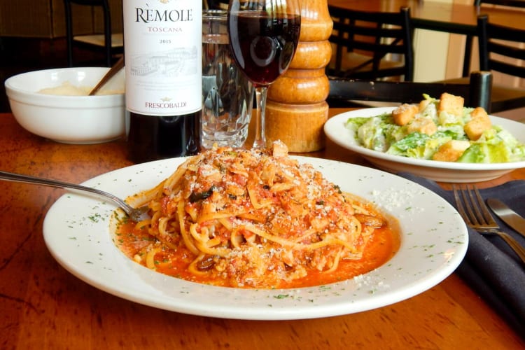 A bowl of linguine next to a salad and wine