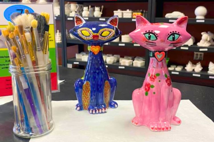 Two painted ceramic cats next to paint brushes