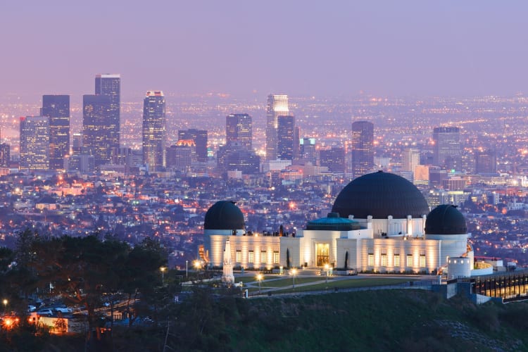 A building on a hill next to an illuminated city skyline at night