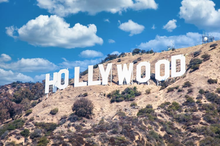 The Hollywood sign on a greenery-covered hill under a blue sky with clouds