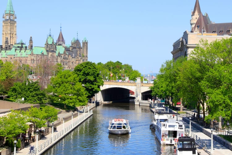 A boat on a canal with trees, a bridge and buildings around it