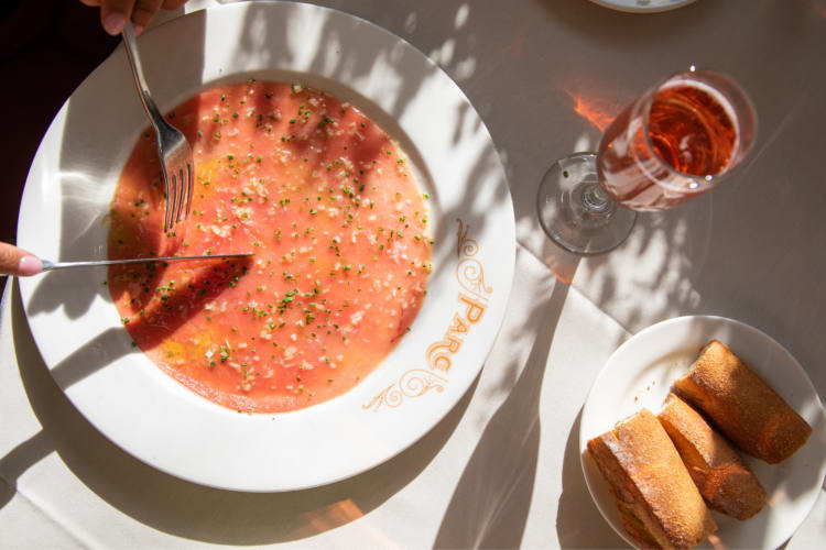 A plate of salmon next to a bowl of bread and glass of rose wine