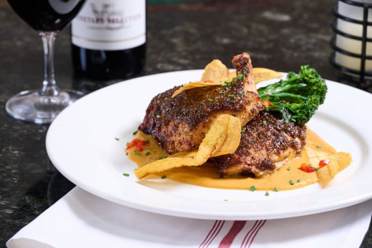 Jerk seasoned chicken, broccolini and fried plantains next to a wine glass