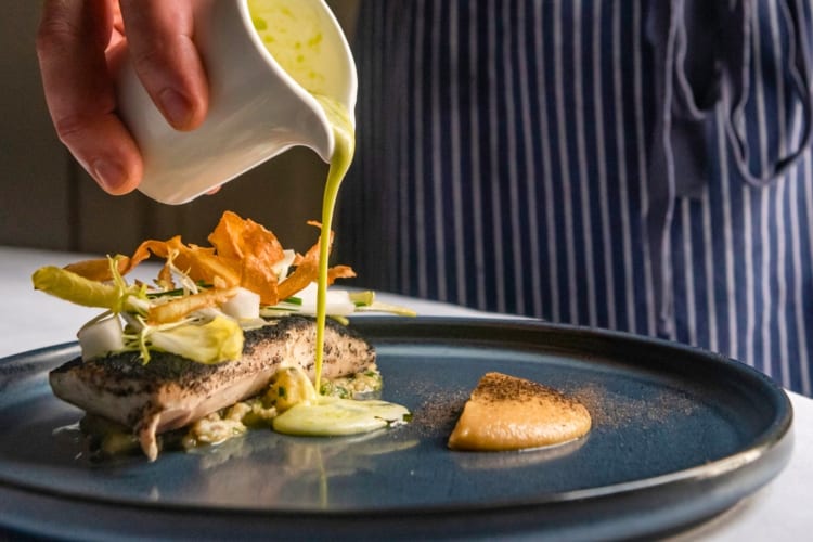 A green sauce being poured onto a plated dish