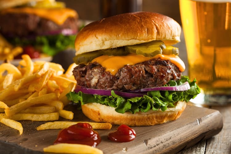 Bison burger on a serving board with fries and tomato sauce