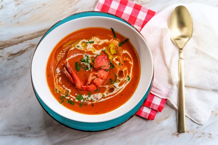 A bowl of lobster bisque next to a gold spoon and napkins