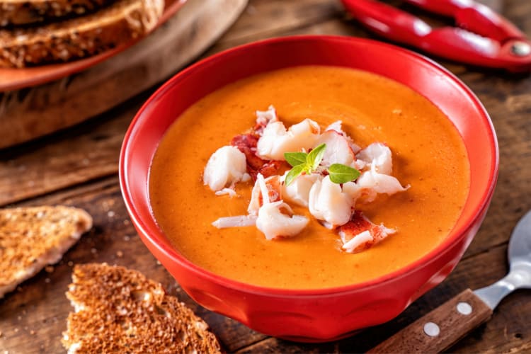 A bowl of soup with lobster next to pieces of bread