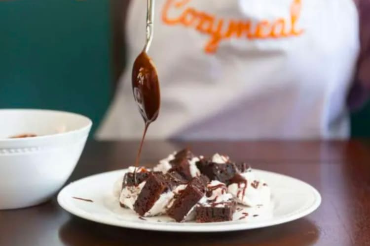 A person pouring chocolate sauce on a brownie dessert