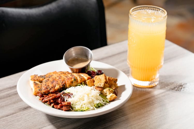 A chicken salad with pecans and cheese next to an orange drink