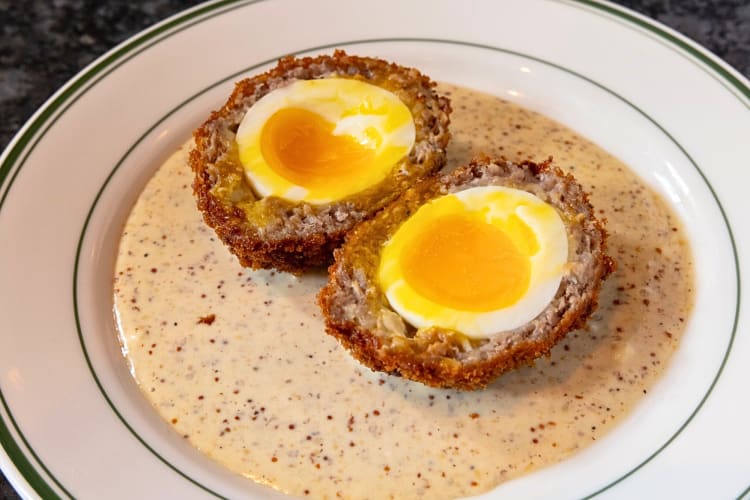 Scotch egg cut in half laying on a bed of sauce, from Bog & Barley