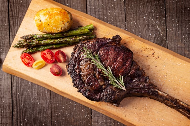 Bone-in ribeye steak with a side of tomatoes, asparagus and a baked potato