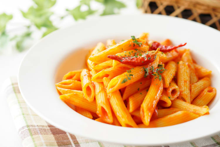 Bowl of cooked penne pasta with herbs on top ready to be eaten