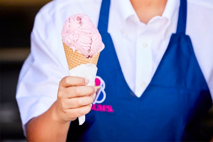 A person in a blue apron holding a strawberry ice cream cone
