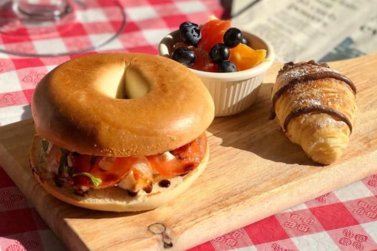 A bagel, a croissant and some fruit on a wooden cutting board