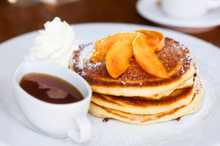 Pancakes with peaches and cream next to a jug of syrup