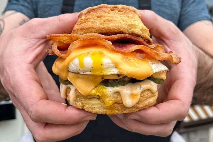 Breakfast smash sandwich loaded with a burger patty, fried egg, cheese, pickle on a buttermilk biscuit 