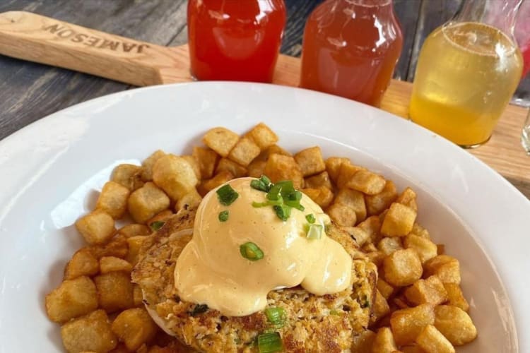 A breakfast dish with home fries next to juices in small glasses