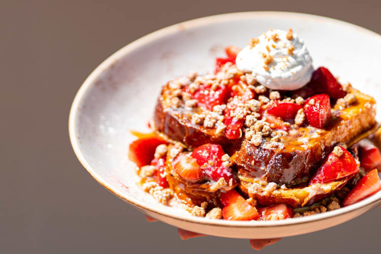 A bowl with French toast, strawberries, and whipped cream