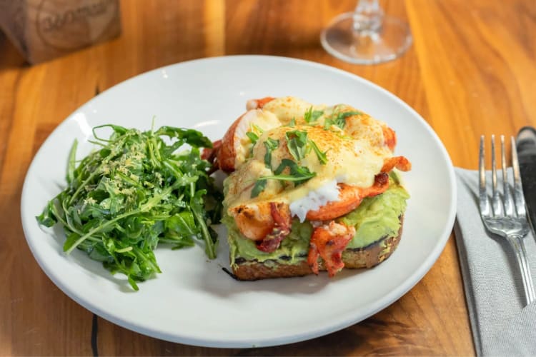 Lobster eggs Benedict on avocado toast next to arugula