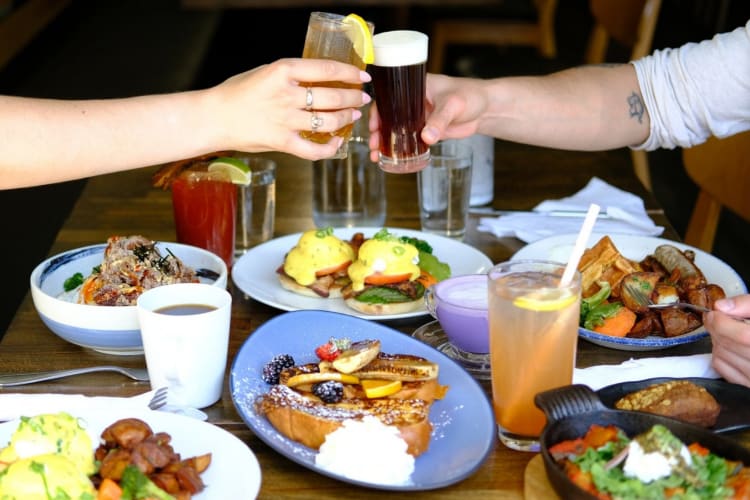 Two people cheersing glasses above a table with breakfast dishes