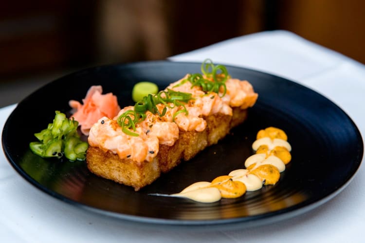 A  salmon and crispy rice dish on a black plate