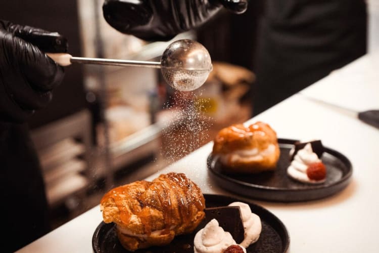 Close-up shot of a chef's hands sprinkling icing sugar over a dessert at the D.C. restaurant Bronze