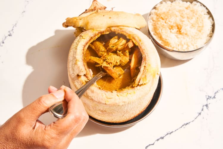 A person taking curry from a hollowed coconut