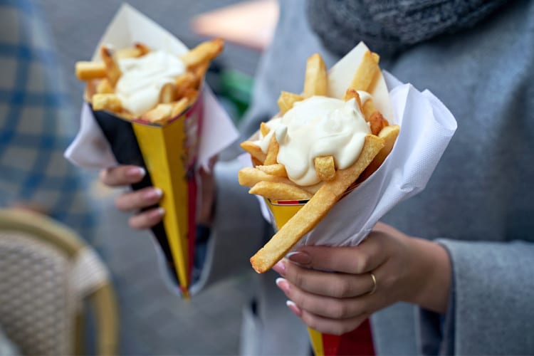 A person holding two cones of fries with mayonnaise
