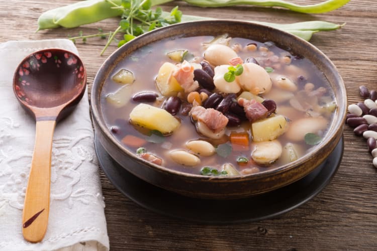 A bowl of soup with beans, meat and vegetables
