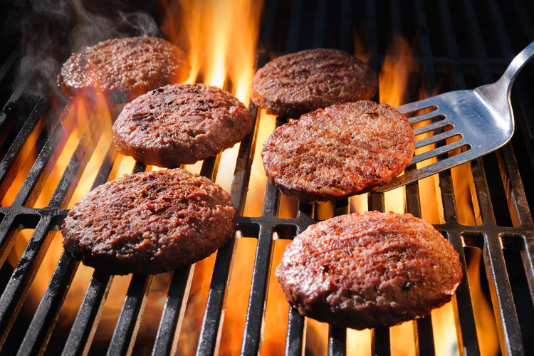 Six patties being cooked on a grill with flames