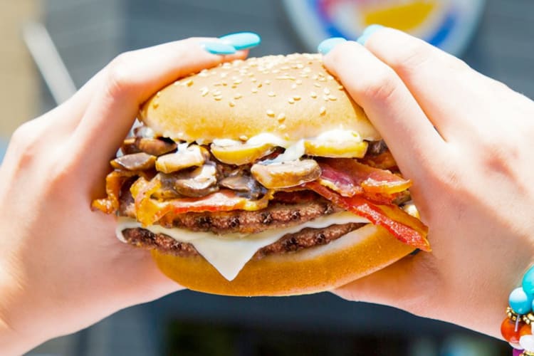 A person holding a burger with cheese and mushrooms