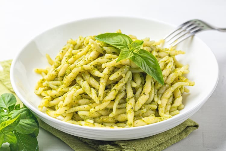 Busiate al pesto trapanese in a white bowl topped with basil leaves