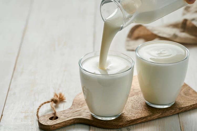 Buttermilk being poured into a glass next to a full glass of buttermilk