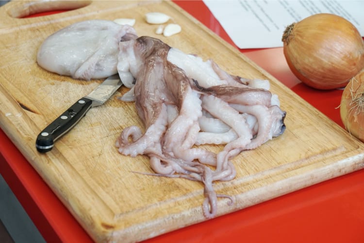 A whole squid on a chopping board, ready to be prepared.