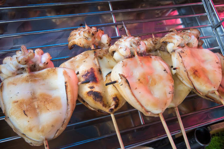 Squid skewers cooking over a grill.