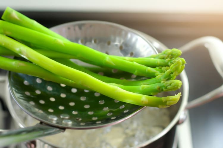 Asparagus on a spoon being lifted out of boiling water