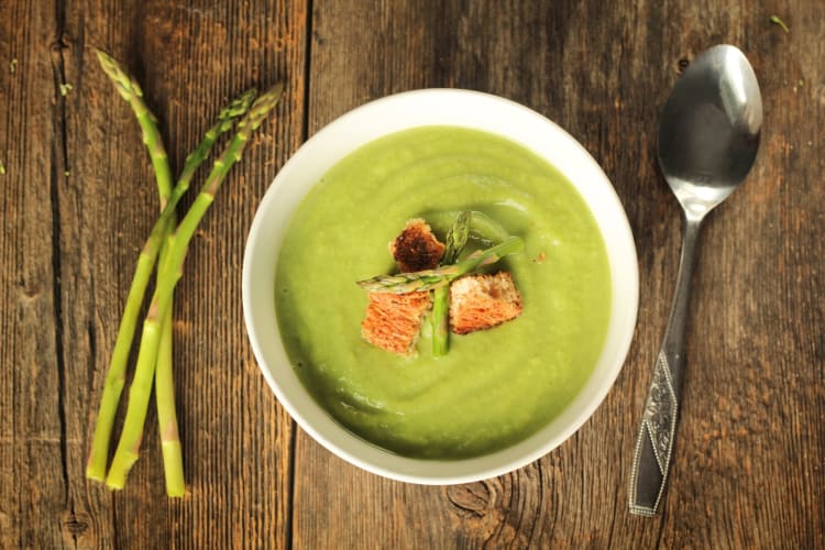 A bowl of asparagus soup on a wooden surface