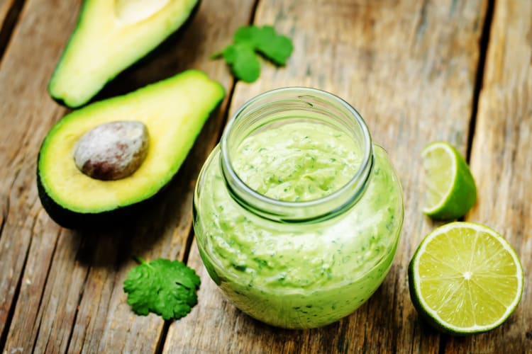 A jar of avocado puree next to halved avocados and lime